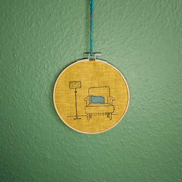 This is a one-off design in my ‘interiors’ collection. Designed and hand stitched by me using DMC threads onto a mustard background with a Harris tweed cushion on the armchair. The back of the hoop is covered in a blue wool felt and is ready to hang using the contrasting teal crocheted loop.  Only one available.