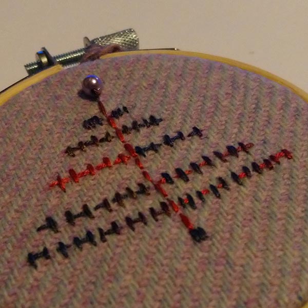 A modern Christmas tree stitched with variegated thread onto a lavender Harris tweed fabric, topped with a little pearl bead. Supplied with a crocheted yarn loop in a contrasting colour. 