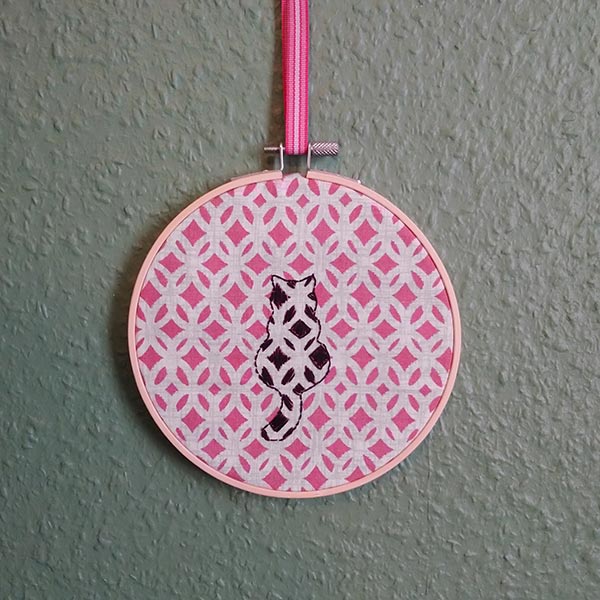One for the cat lovers! A black geometric cat embroidered onto patterned dusky pink fabric.  The back of the hoop is covered with real wool felt in a rather fetching shade of plum! The hoop is supplied with contrasting ribbon hanging loop. 