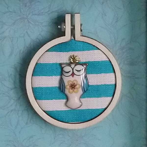 Owl charm stitched with DMC metallic thread onto recycled fabric in a mini embroidery hoop.  Mounted onto a subtle print background and framed in a shadow box frame. Freestanding or wall hanging. Only one available.