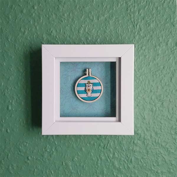 Owl charm stitched with DMC metallic thread onto recycled fabric in a mini embroidery hoop.  Mounted onto a subtle print background and framed in a shadow box frame. Freestanding or wall hanging. Only one available.